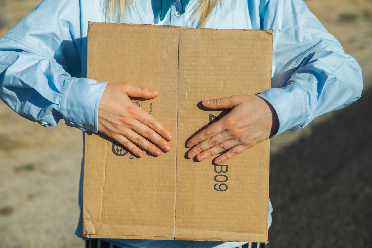 A person holds a cardboard box outdoors, emphasizing minimalism and delivery concept.
