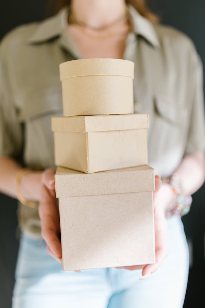 A woman holding a stack of plain cardboard boxes against a blurred background.