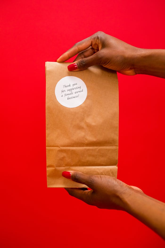 Hands holding a kraft paper bag with thank you sticker on a vibrant red background.
